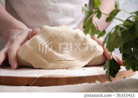 Women's hands knead the dough from wheat flour 76353453