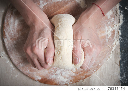 Women's hands knead the dough from wheat flour 76353454
