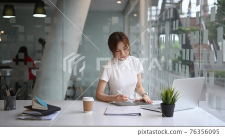 Successful businesswoman sitting in modern workplace and concentrate working on digital tablet. 76356095