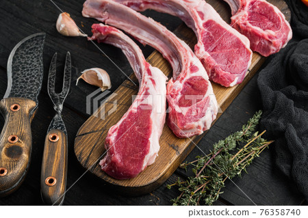 Raw Lamb chops , with ingredients carrot orange, herbs, on black wooden table background Raw Lamb chops , with ingredients carrot orange, herbs, on black wooden table background 76358740