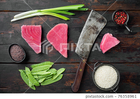 Raw tuna steak, fresh red tuna fillet with ingredients, green pea, sesame and spices, and old butcher cleaver knife, on old dark wooden table background, top view flat lay Raw tuna steak, fresh red tuna fillet with ingredients, green pea, sesame and spices, and old butcher cleaver knife, on old dark wooden table background, top view flat lay 76358961