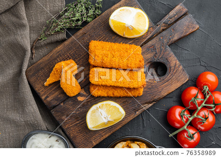 Fried fish finger stick or french fries fish with sauce, on wooden cutting board , on black background , on black wooden table background, top view flat lay Fried fish finger stick or french fries fish with sauce, on wooden cutting board , on black background , on black wooden table background, top view flat lay 76358989