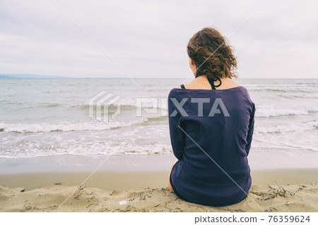 girl sitting on the sand on the shore of the beach looking at the horizon of the sea 76359624