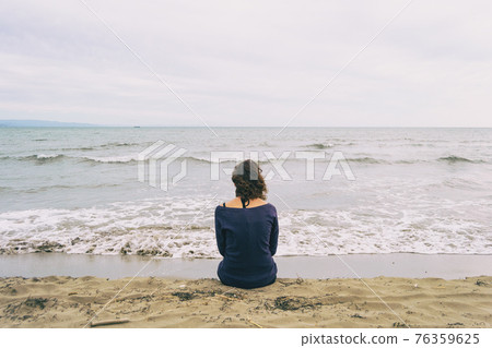 girl sitting on the sand on the shore of the beach looking at the horizon of the sea 76359625