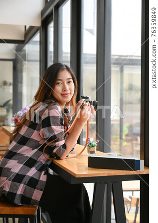 Portrait of cheerful young female photographer holding her digital camera and smiling to camera. Portrait of cheerful young female photographer holding her digital camera and smiling to camera. 76359849