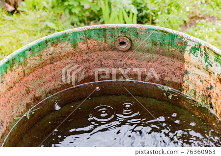 Old rusty rain barrel with water in the rain Old rusty rain barrel with water in the rain 76360963