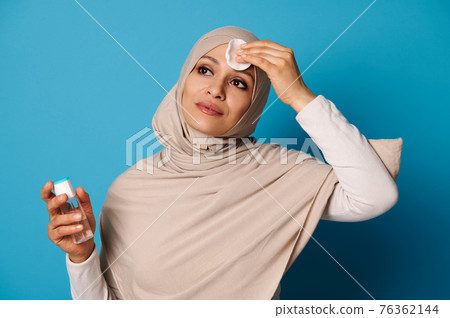 Attractive muslim woman removing makeup from her face using micellar water and cotton pad. Skin care concepts Attractive muslim woman removing makeup from her face using micellar water and cotton pad. Skin care concepts 76362144