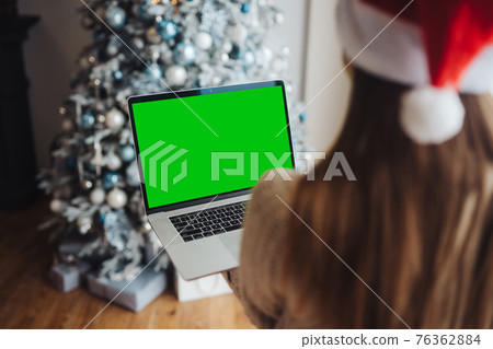 Female wearing santa hat while speaking with online friend on laptop 76362884