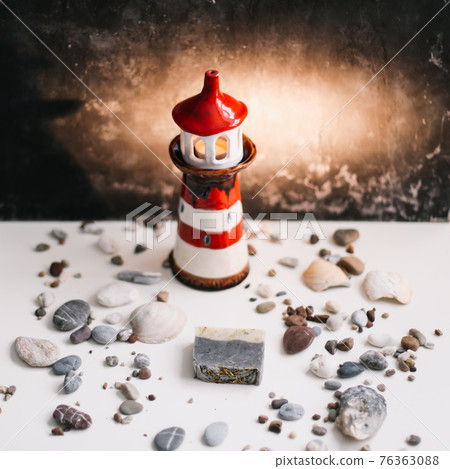 A small decorative lighthouse with sea shells and stones on a dark background. Summer, holidays and vacation concept 76363088