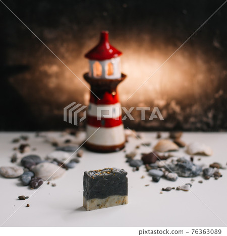 A small decorative lighthouse with sea shells and stones on a dark background. Summer, holidays and vacation concept A small decorative lighthouse with sea shells and stones on a dark background. Summer, holidays and vacation concept 76363089