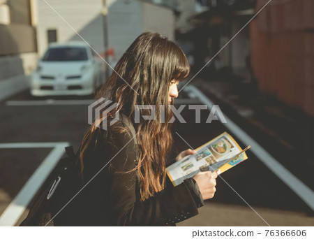 Profile of a long-haired woman walking while reading a magazine 76366606