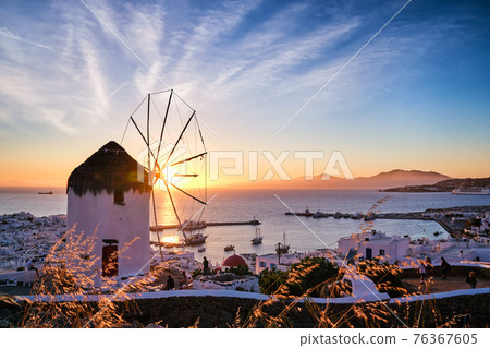 Famous traditional white windmill overlook port and harbor of Mykonos, Cyclades, Greece at sunset sky. Beautiful sky, sun, sea, horizon, town, island 76367605