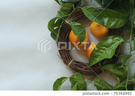 Clementines tangerines, twig with green leaves as spring decor and handmade  wreath from twig on gray paper background. 76368992