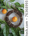 Clementines tangerines, twig with green leaves as spring decor and handmade  wreath from twig on gray paper 76368993