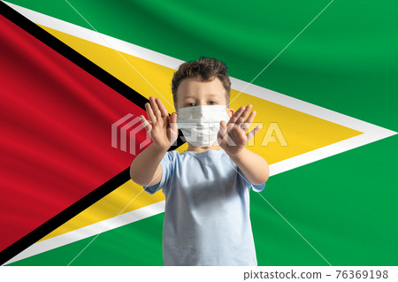 Little white boy in a protective mask on the background of the flag of Guyana. Makes a stop sign with his hands, stay at home Guyana Little white boy in a protective mask on the background of the flag of Guyana. Makes a stop sign with his hands, stay at home Guyana 76369198