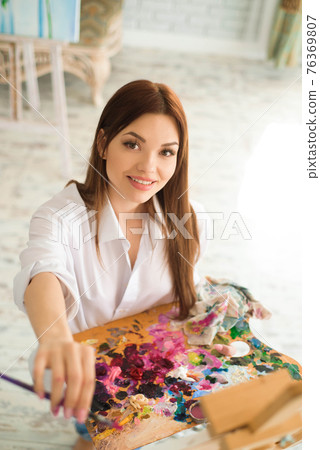 Cute girl artist paints on canvas painting on the easel. Model in the studio. 76369807