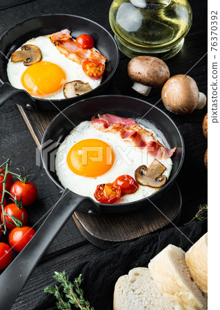 Scrambled eggs in frying pan with pork lard, bread and green feathers in cast iron frying pan, on black wooden table background Scrambled eggs in frying pan with pork lard, bread and green feathers in cast iron frying pan, on black wooden table background 76370392