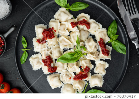 Appetizing ravioli with tomato sauce, cheese and basil with basil parmesan and tomatoe on black plate, on black background , top view flat lay 76370417