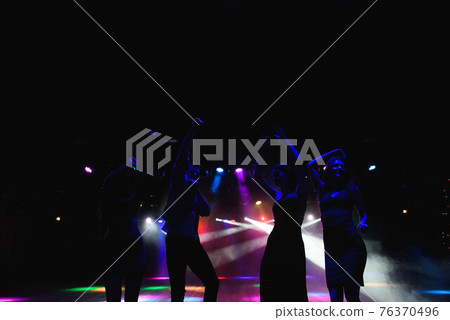 Silhouettes of dancing people in club in front of bright stage lights - disco concept. 76370496