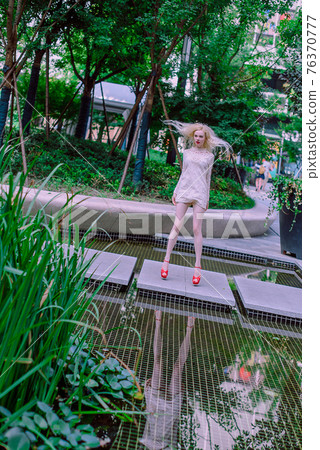 Beautiful young blonde smiling happy woman with red lips in red shoes in a white dress play near a fountain in a summer day Beautiful young blonde smiling happy woman with red lips in red shoes in a white dress play near a fountain in a summer day 76370777