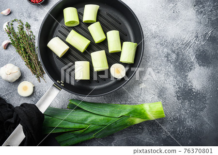 Raw braised Leeks on grill pan uncooked with herbs ingredients , on textured grey background top view with space for text. 76370801
