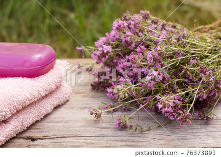 Towel with thyme flowers and soap on wooden background. Towel with thyme flowers and soap on wooden background. 76373891