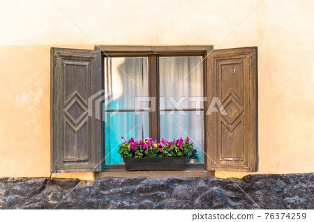 Bavarian or austrian wooden window with red geranium flowers on house in Europa 76374259