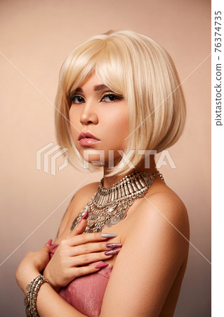 beauty portrait of a young beautiful blonde girl of Asian or Egyptian appearance on a pink solid background. beauty portrait of a young beautiful blonde girl of Asian or Egyptian appearance on a pink solid background. 76374735
