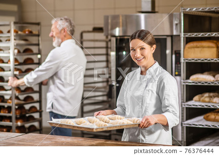 Woman with tray of croissants man with rack of bread Woman with tray of croissants man with rack of bread 76376444