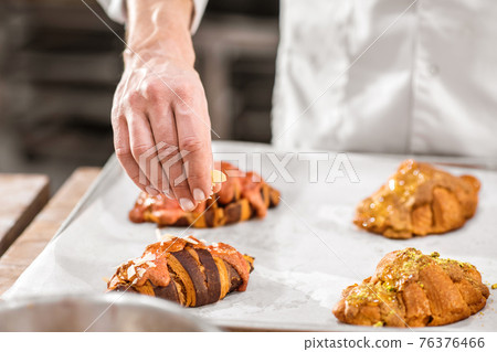 Hand sprinkling the croissants with nut chips Hand sprinkling the croissants with nut chips 76376466