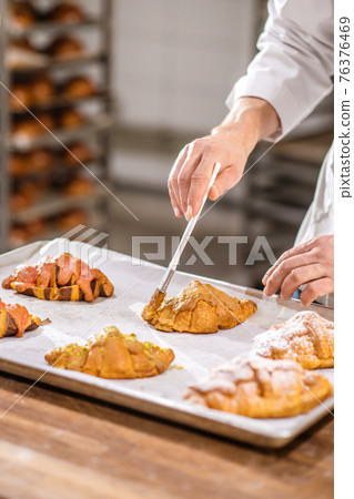Pastry chefs hand with brush over tray of croissants Pastry chefs hand with brush over tray of croissants 76376469