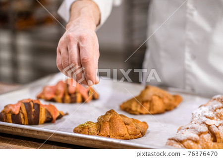 Confectioner hand decorating surface of cooked pastries 76376470