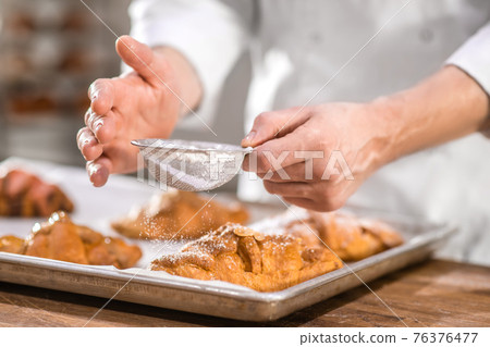Chefs hands with small sieve over baking Chefs hands with small sieve over baking 76376477