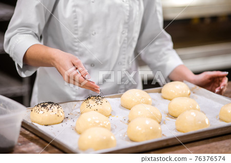 Female hand sprinkling grains on surface of buns 76376574
