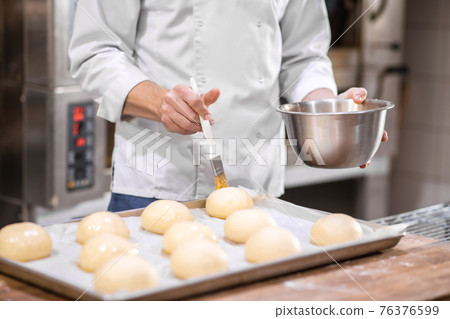 Male hands covering rolls with confectionery glaze 76376599