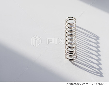 Metal mainspring on white background. Flexible chrome tube. Corrugated object on geometrical banner with copy space on hard sunlight and shadow. 76376638