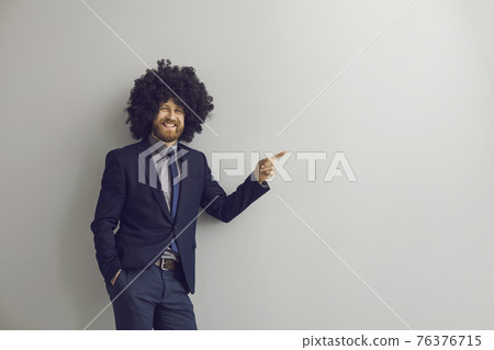 Loudly laughing business man in funny afro curly hair wig pointing at something 76376715