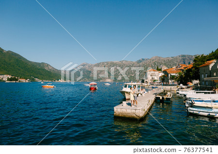 A man and a woman standing and hugging each other on the pier near the boats in old town of Perast A man and a woman standing and hugging each other on the pier near the boats in old town of Perast 76377541