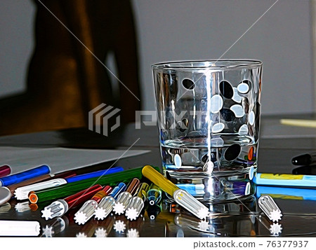 A glass of water decorated with black and white spots, and colored markers on a table. Digital painting. A glass of water decorated with black and white spots, and colored markers on a table. Digital painting. 76377937
