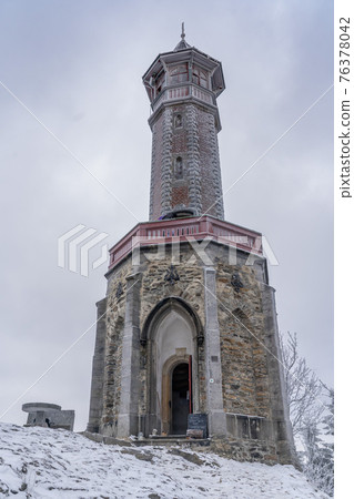 Lookout tower Stepanka on the border of Krkonose and Jizera Mountains. Winter overcast day, sky with clouds, trees covered with snow. 76378042