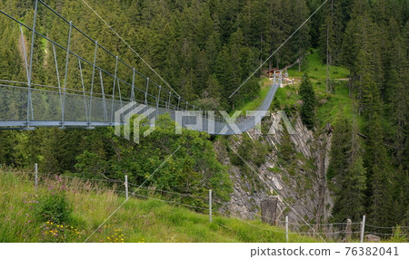high suspension bridge between mountains trees and rocks 76382041
