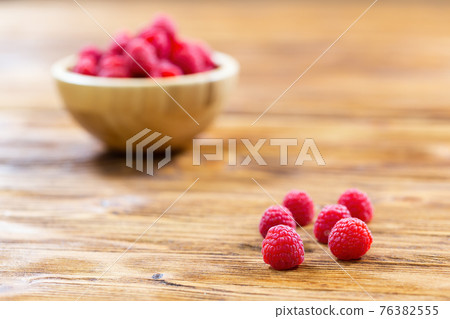 Pile of fresh raspberries lying on table with full bowl in background Pile of fresh raspberries lying on table with full bowl in background 76382555