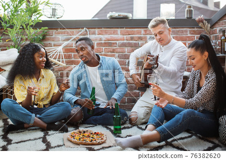 Diverse friends relaxing with pizza and alcoholic drinks 76382620