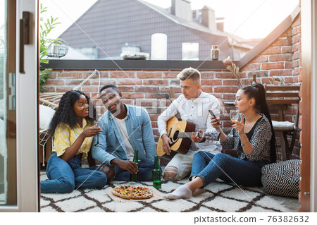 Multiracial friends playing guitar, drinking and eating 76382632