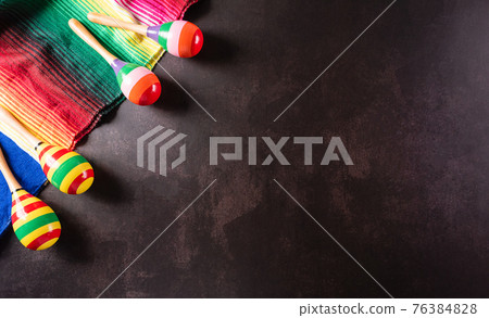 Cinco de Mayo holiday background made from maracas, mexican blanket stripes or poncho serape on dark stone background. 76384828