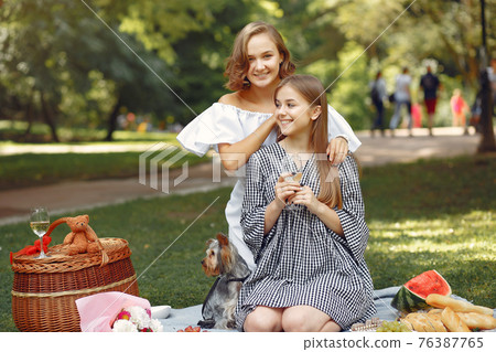 Two cute girls in a park playing with little dog Two cute girls in a park playing with little dog 76387765