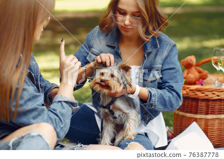 Two cute girls in a park playing with little dog Two cute girls in a park playing with little dog 76387778