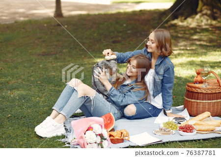 Two cute girls in a park playing with little dog Two cute girls in a park playing with little dog 76387781