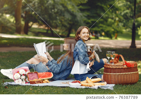 Two cute girls in a park playing with little dog Two cute girls in a park playing with little dog 76387789