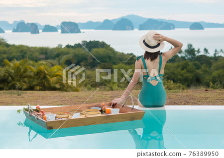 Happy young woman in green swimsuit having Floating Breakfast tray in luxury pool hotel, girl with hat enjoy in tropical resort. Relaxing, Exotic summer travel, holiday, vacation and tropical 76389950
